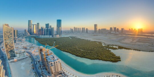 Skyscrapers on Al Reem and Al Maryah Island in Abu Dhabi at sunset timelapse from above. Aerial citiscape from Al Reem Island with modernd buildings. Orange sky and sun reflected on glass surface