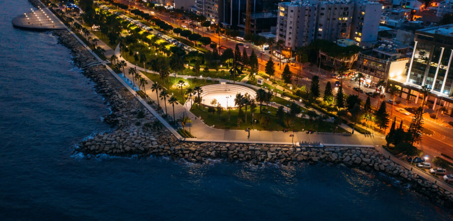 Aerial night panorama of Limassol, Cyprus waterfront. Famous mediterranean city resort in evening with Molos Park, promenade or embankment and buildings, from above view.
